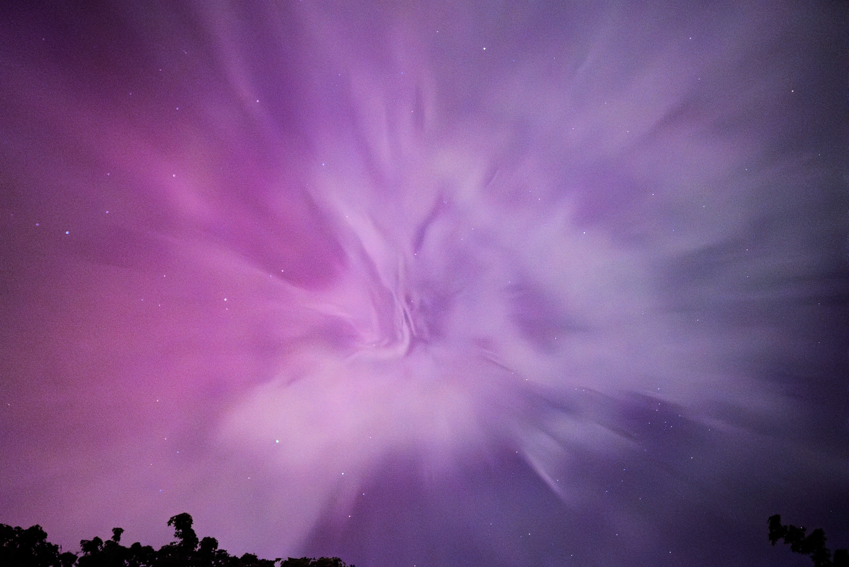 A vivid, ethereal capture of a night sky. The image showcases swirling clouds and distant stars set against a mesmerizing palette of purple and pink.